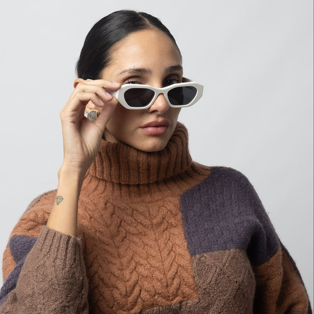 Woman wearing a patterned sweater holding sunglasses against a plain background