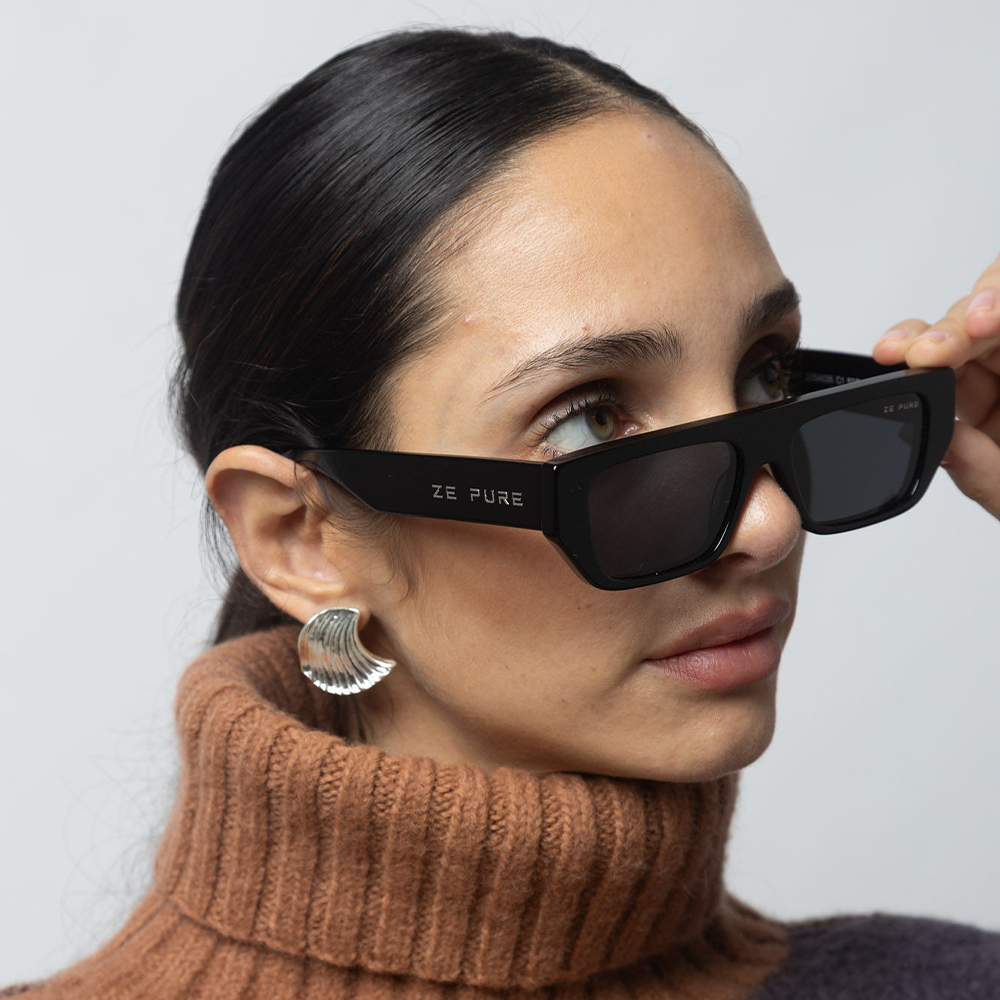 Woman wearing black sunglasses with 'ZE PURE' branding, wearing a brown turtleneck sweater.