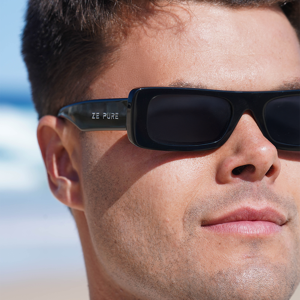 Close-up of a man wearing black sunglasses with 'ZE PURE' branding, against a blurred outdoor background.
